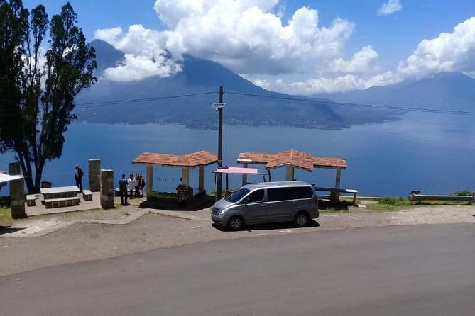 An Antigua Panajachel shuttle minivan at a scenic overlook with Lake Atitlán in the background.