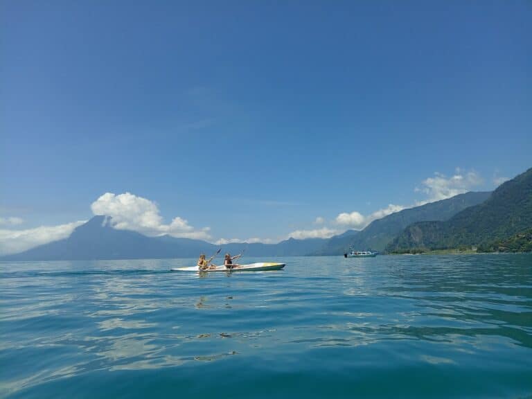 Dos chicas navegan en kayak por el lago de Atitlán con los volcanes al fondo.