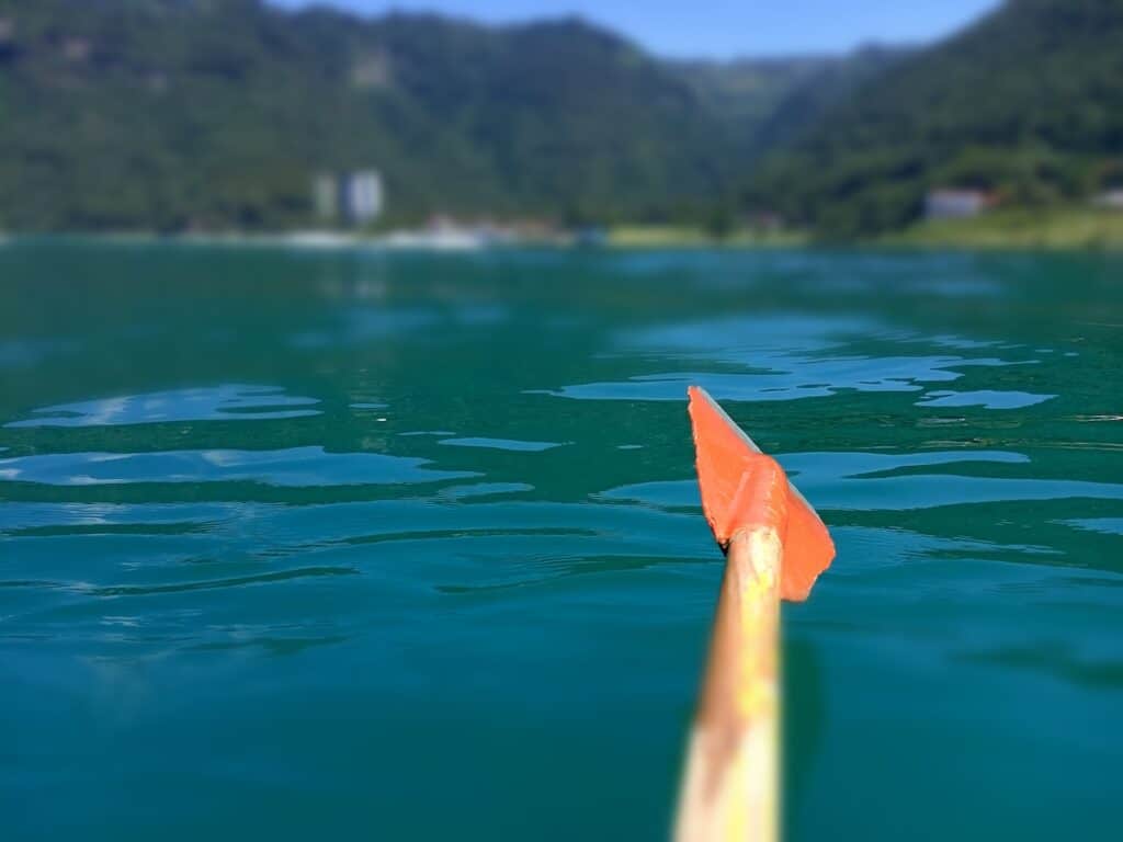 Un remo se extiende sobre el agua que refleja el verde de los acantilados circundantes. Al fondo, se ve la orilla verde y borrosa.