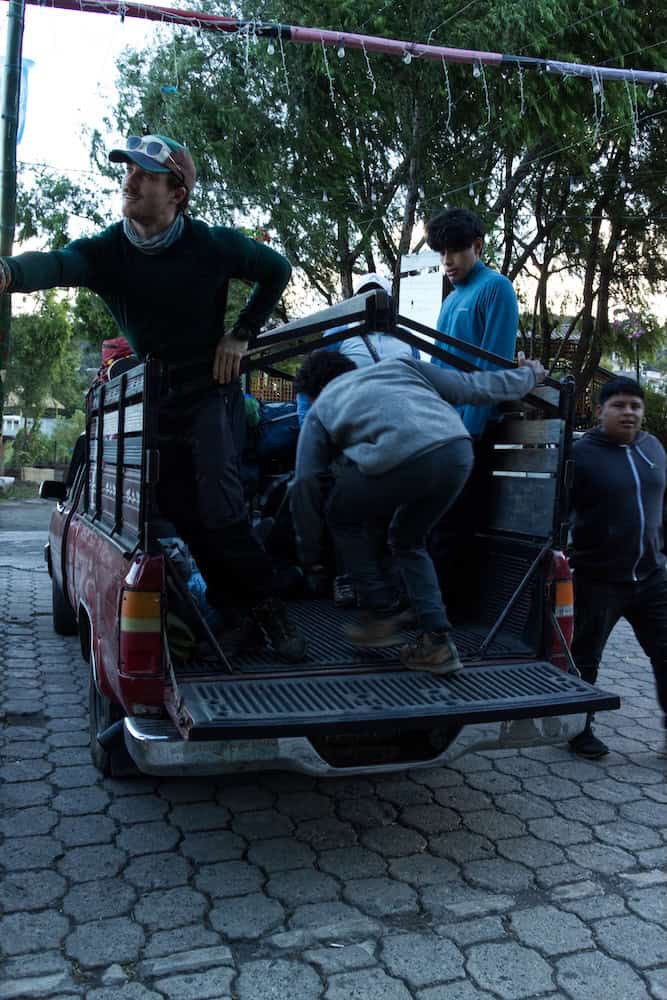 Hikers board a pickup with their hiking packs.