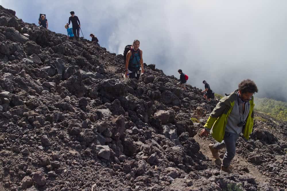 A group of hikers zigzags up a steep slope covered in chunks of volcanic rock.