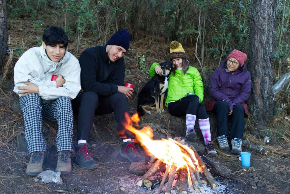 A group of hikers huddle around a campfire on one of the flat camping platforms in the Atitlán forest campsite.